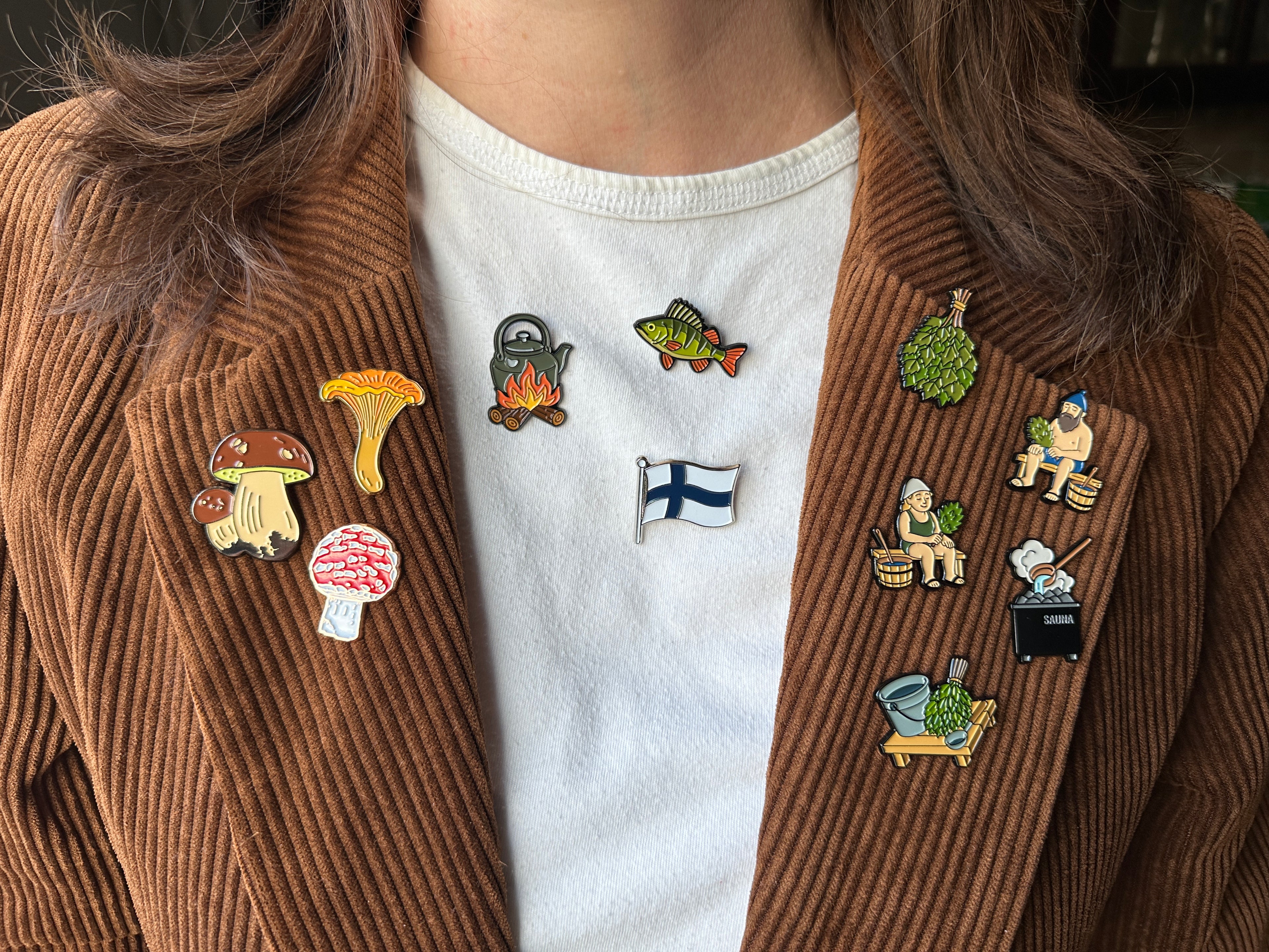 Person wearing a brown jacket with various pins on a white shirt